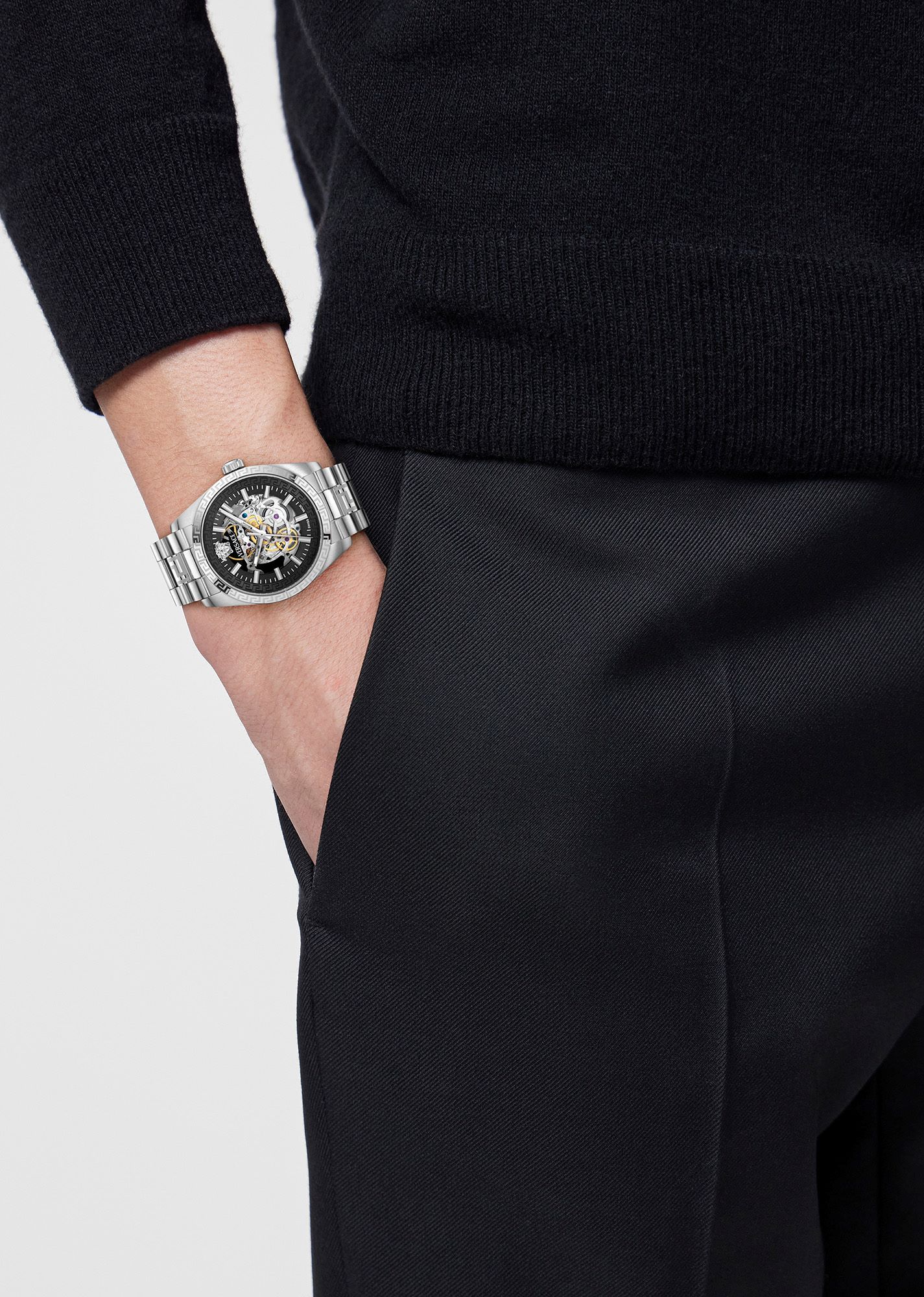 A sleek Versace automatic watch with a black dial and silver bracelet, worn on the wrist over dark clothing.