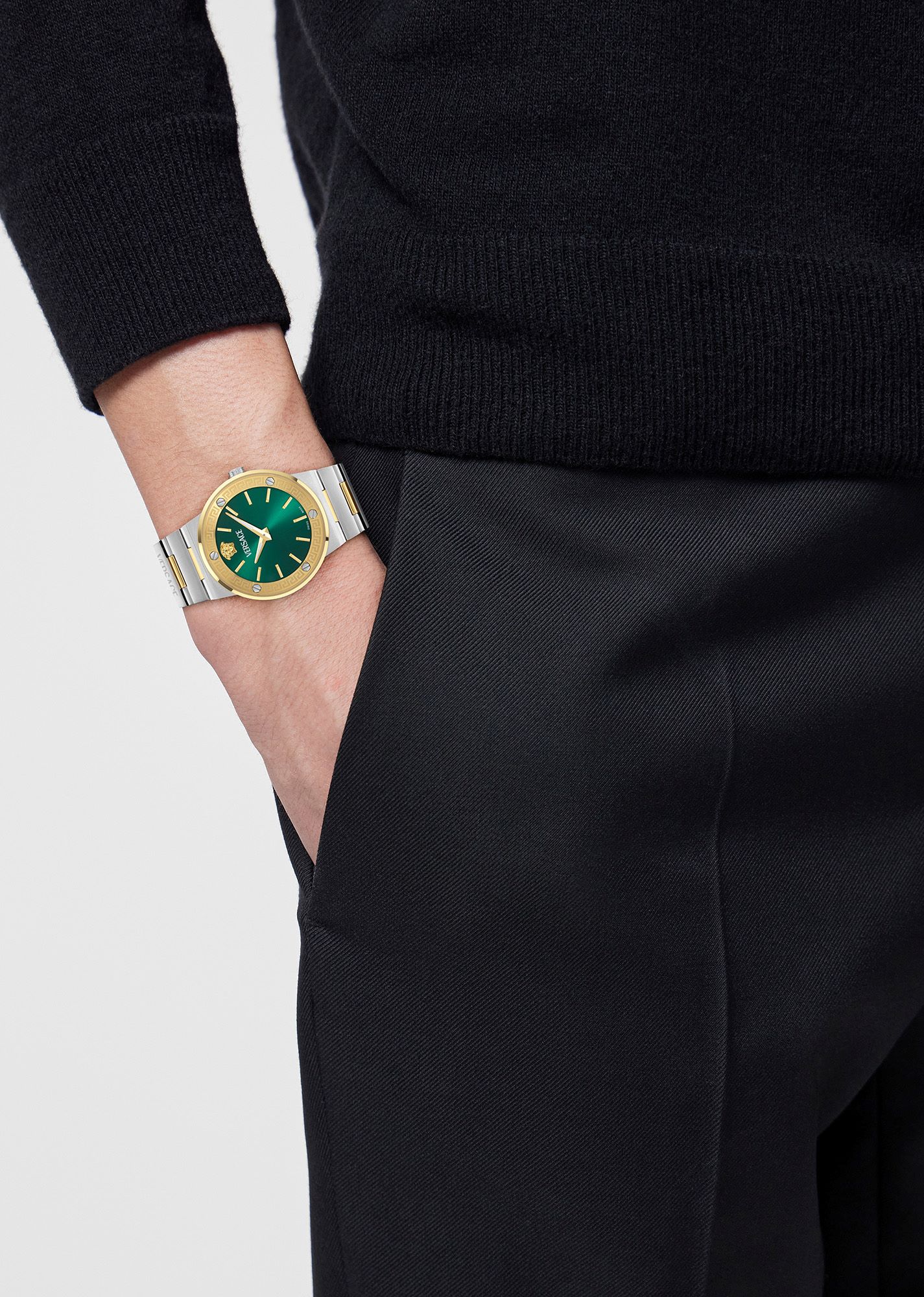 Green dial watch with a gold bezel and silver bracelet worn on a person's wrist, paired with a black sweater and pants.